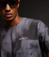 Remera deportiva negra con estampado manchado en gris y lettering en el pecho. Confeccionada en tejido dry de poliéster y elastano, con cuello redondo y mangas cortas.