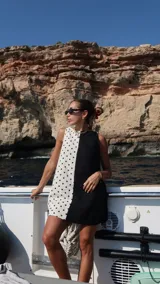 Vestido corto sin mangas, con escote recto y corte a la rodilla. Presenta un diseño bicolor, con un lado blanco con lunares negros y otro lado negro liso.