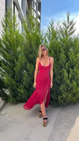 Vestido largo de crepé color fucsia, con escote corazón, tirantes finos y aberturas laterales en la cintura. La falda presenta un diseño con frunces laterales y una abertura frontal que deja ver la pierna.