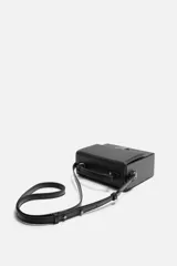Bandolera rígida negra en formato caja con cierre metálico y asa de hombro ajustable.