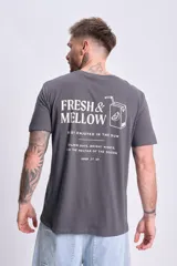 Remera gris de manga corta con estampa en la espalda que incluye el texto 'Fresh & Mellow', la frase 'Best enjoyed in the sun' y el dibujo de un jugo de naranja.