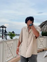 Camisa beige de corte amplio, con cuello clásico, manga corta y cierre frontal con botones.