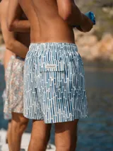 Short de baño azul con estampado de líneas verticales en tonos de azul y blanco. Tiene elástico en la cintura, cordón ajustable, tres bolsillos y mesh interior hipoalergénico.
