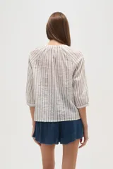 Camisa blanca de algodón con rayas verticales en tono beige/tostado y detalles de bordado tipo ojal a lo largo de las rayas. Presenta cuello mao con abertura en V y botones frontales, y mangas 3/4 con ligero volumen.