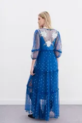 Vestido largo de tul bordado color azul con hilo de lurex y lentejuelas plateadas. Tiene escote en V cruzado, mangas 3/4 con volados y puños elásticos, frunces en la cintura y viso a tono.