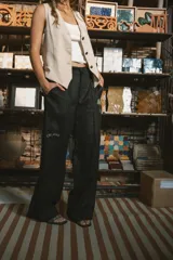 Pantalón de vestir negro de tiro alto, corte recto y pierna ancha. Presenta pliegues frontales y bolsillos laterales.