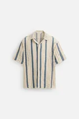 Camisa de crochet color beige con rayas verticales azules, cuello bowling, manga corta y cierre frontal con botones.
