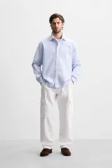 Camisa celeste con rayas verticales blancas, de corte regular, cuello solapa, manga larga con puños abotonados y cierre frontal con botones.