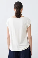 Blusa color beige con textura de lunares en relieve, cuello redondo y mangas cortas.