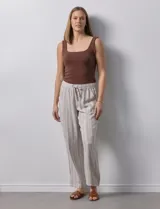 Pantalón de lino a rayas verticales color beige y blanco, con pretina ancha elastizada, lazo de ajuste y bolsillos inclinados.