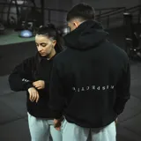 Canguro negro oversize unisex de algodón con felpa, con bordado de la palabra "Perspective" al revés en la espalda y en la manga.