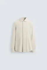 Camisa color beige de corte slim fit, confeccionada en tejido elástico con cuello italiano abierto, manga larga con puños abotonados y cierre frontal con botones.