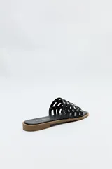 Sandalia baja negra con diseño entrelazado y apliques metálicos.