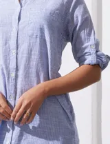 Camisola larga de algodón color blanco, marca Dash. Tiene cuello con solapa, abertura central con botones, bolsillo aplicado en el pecho, mangas regulables con presilla y botón, y bolsillos laterales en la costura.
