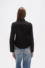 Camisa blanca de algodón, entallada, con cuello camisa y cierre frontal de botones. Presenta mangas largas con puños sencillos.