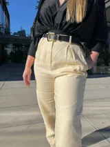 Pantalón de vestir color amarillo claro, de corte recto, con bolsillos laterales y traseros. Se ajusta a la cintura con cinturón de cuero marrón.