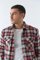 Sobrecamisa de algodón para hombre con interior de corderito, estampado a cuadros en tonos negro, blanco y azul. Tiene cierre de botones, bolsillos tipo cartera y logo en goma. El modelo usa talle M.