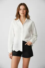 Camisa blanca de algodón con bordado tipo broderie, corte holgado, cuello camisero y cierre frontal con botones.