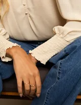 Blusa color beige de gasa con escote en V, apliques de botones y detalle de punto smock en hombro y puño.