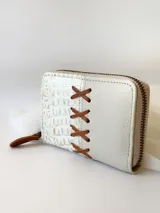 Billetera pequeña de cuero color crema, con cierre metálico y monedero interno. Presenta un diseño de cruces marrones en el frente y textura símil cocodrilo en un lateral.