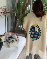 Ruana de lana merino color crudo, tejida y bordada a mano con el escudo de Uruguay en la espalda. Tiene calce holgado y flecos en el ruedo.