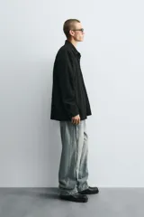 Camisa negra de denim de algodón con textura irregular, corte relaxed fit, cuello solapa, manga larga con puños abotonados y cierre frontal con botones.