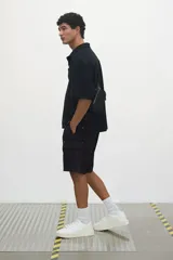 Short cargo negro de popelina de algodón, con cintura elástica ajustable con cordón, bolsillos laterales, bolsillos cargo con solapa y botón a presión en piernas y traseros, y aberturas laterales en el bajo.