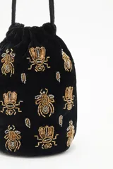 Cartera tipo bombonera negra de terciopelo con bordado de lentejuelas y canutillos dorados con forma de insectos. Tiene cordón de ajuste con borlas de canutillos dorados y correa de mano.