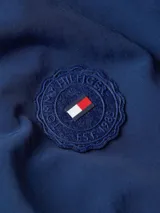 Rompevientos azul de Tommy Hilfiger, corto, con cuello alto, cierre de cremallera, dos bolsillos laterales, detalles distintivos de la marca y logo engomado bordado en la manga.
