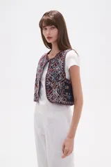 Chaleco sin mangas, sin abroches, con escote redondo. Confeccionado en tejido oscuro con bordados geométricos y florales en tonos rojos, blancos, azules y mostaza, con apliques de cuentas.