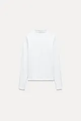 Camiseta blanca de manga larga con cuello alto y corte ajustado.