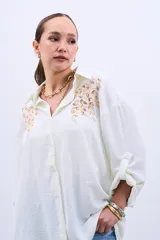 Camisa color crudo con bordado de lentejuelas doradas en el frente, de corte holgado y mangas largas con lazo en los puños.