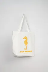 Tote bag blanca con estampado de un caballito de mar en color naranja y texto en la parte inferior.