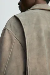 Cazadora de hombre color verde oliva, confeccionada en piel con acabado ante. Presenta un corte boxy fit, cuello solapa, cierre frontal de cremallera, bolsillos delanteros y elásticos en puños y bajo.