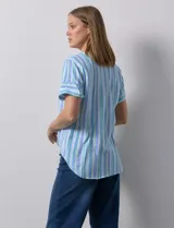Blusa de algodón estampado a rayas verticales en tonos celeste, azul y verde. Tiene cuello a la base, escote en V con bordado y botones. Terminación de ruedo con nudo.