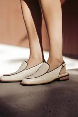 Mocasines slingback negros de cuero con punta cuadrada, ribete en color crudo y hebilla dorada ajustable.