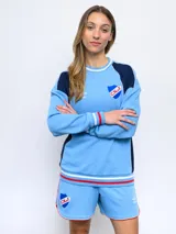 Buzo celeste con mangas azul marino y detalles tricolor en puños y cuello. Escudo del Club Nacional de Football bordado en el pecho.