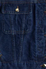 Campera de denim azul oscuro de algodón grueso con cuello redondo y solapa rompevientos guateada con botones ocultos. Modelo de corte holgado con hombros apenas caídos y puños ceñidos con botón. Bolsillos superiores con solapa y botón, bolsillos laterales discretos y trabillas ajustables con botón en el bajo.