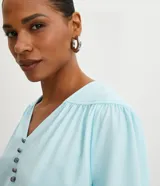 Blusa rosa de poliéster con escote en pico, botones delanteros, manga larga con puños elásticos y pliegues en los hombros.