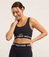Top deportivo negro de microfibra con breteles anchos, copas desmontables, recorte cut-out en el busto y banda elástica con estampado de letras "Keep Moving".