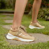 Zapatillas deportivas color beige con detalles dorados, cordones al tono y suela blanca.