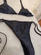 Conjunto de bikini negro con destellos verticales multicolor. El corpiño es de corte triangular con breteles finos regulables y aro metálico en el centro. La bombacha es tipo colaless con tiras laterales regulables.