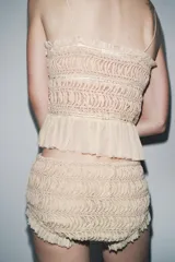 Mini shorts color beige confeccionados en tejido con estructura, tiro alto, cintura elástica y detalle de volantes a tono en los bordes.