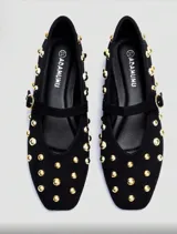Balerinas negras de cuero sintético con tachas doradas, tira sobre el empeine con hebilla dorada y punta redondeada.