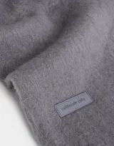 Bufanda rectangular de tejido jacquard en dos tonos de gris, con flecos trenzados en los extremos.