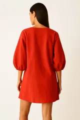 Vestido corto color beige, con escote en V y mangas globo de tres cuartos con elástico en los puños.