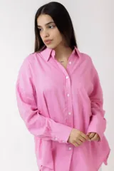 Camisa blanca de lino, de corte holgado, con cuello clásico, cierre frontal con botones, bolsillo en el pecho y mangas largas con puños abotonados.