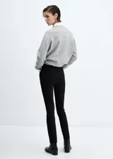 Pantalón negro de corte skinny y largo cropped, confeccionado en tejido fluido con forro interior. Presenta tiro medio, trabillas, bolsillos laterales y traseros de ribete. Cierre frontal con cremallera y botón.