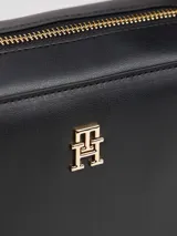 Cartera cruzada tipo cámara de poliuretano negro, con cierre principal de cremallera y monograma TH metálico dorado al frente. Incluye correa larga ajustable con cinta distintiva de rayas azul, blanco y rojo.