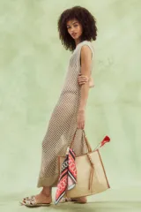 Vestido largo calado color beige, tejido de red con sutil brillo metálico, sin mangas y de cuello redondo.